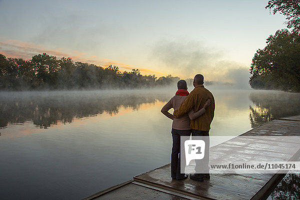 Older couple hugging at foggy river at sunrise