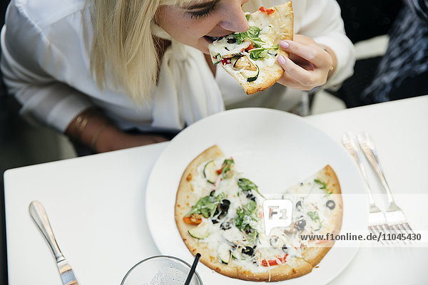Caucasian woman eating slice of pizza in restaurant