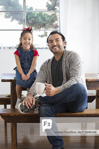 Hispanischer Vater und Tochter lächelnd am Tisch