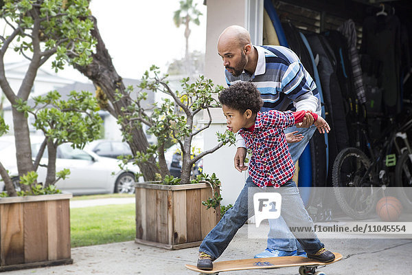 Gemischtrassiger Vater bringt seinem Sohn das Skateboardfahren im Freien bei