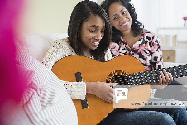 Mother watching daughter play guitar on sofa