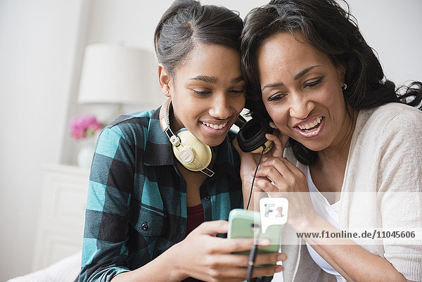 Mutter und Tochter hören über Kopfhörer Musik aus dem Handy