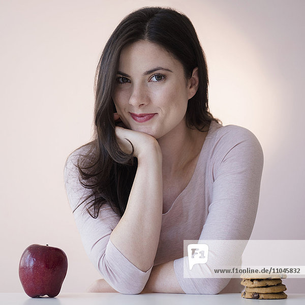 Kaukasische Frau wählt zwischen Apfel und Keksen als Snack