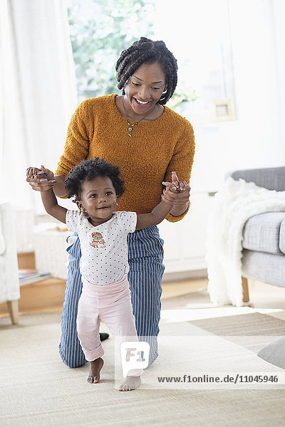 Schwarze Mutter hilft ihrer kleinen Tochter beim Laufen lernen
