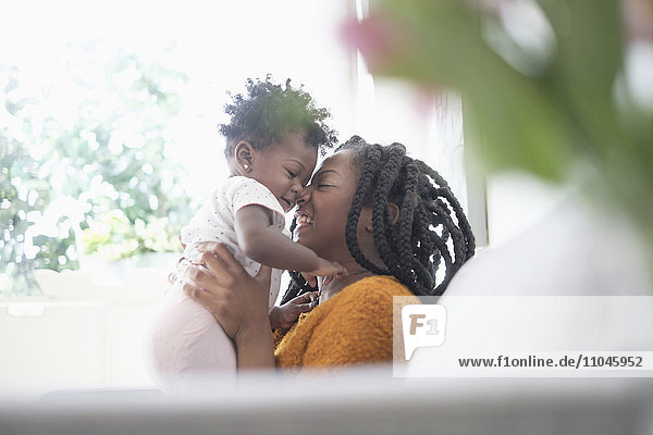 Schwarze Frau reibt sich die Nasen mit ihrer kleinen Tochter auf dem Sofa