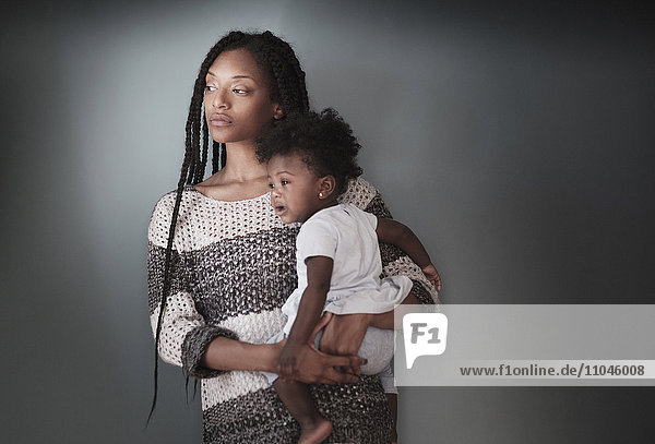 Nachdenkliche schwarze Frau steht und hält ihre kleine Tochter