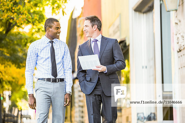 Businessmen walking on sidewalk carrying paperwork