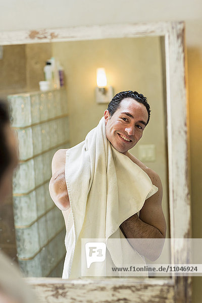 Naked Hispanic man drying with towel in mirror
