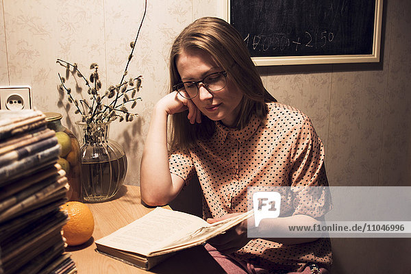 Kaukasische Frau liest ein Buch am Küchentisch