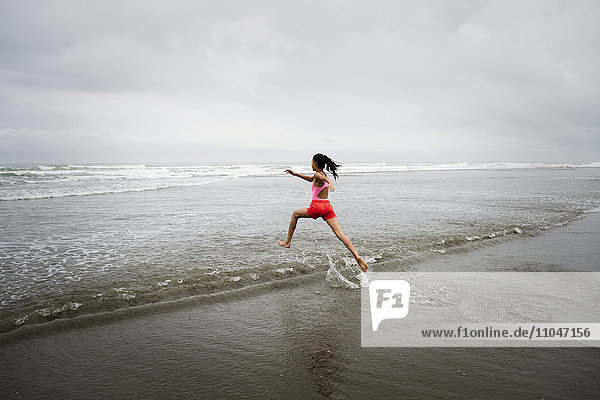 Mixed race girl running into ocean on beach