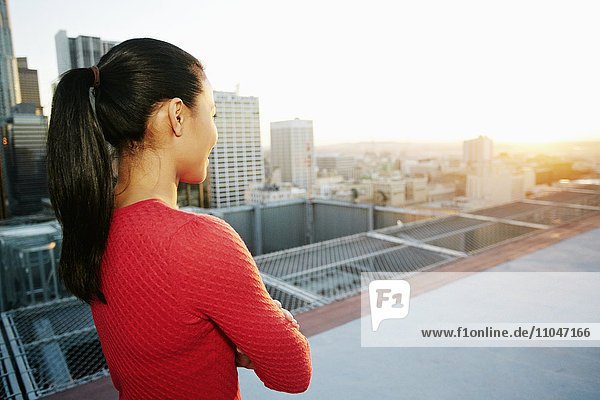 Gemischtrassige Frau beobachtet den Sonnenuntergang auf dem Dach einer Stadt