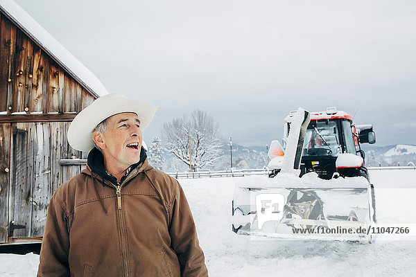 Kaukasischer Bauer und Traktor auf einem verschneiten Feld