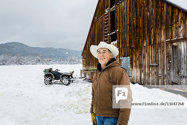 Kaukasischer Bauer lächelt in der Nähe einer verschneiten Scheune