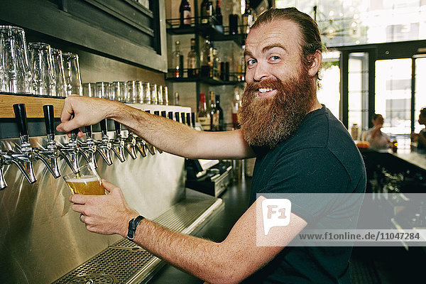 Smiling Caucasian bartender pouring beer