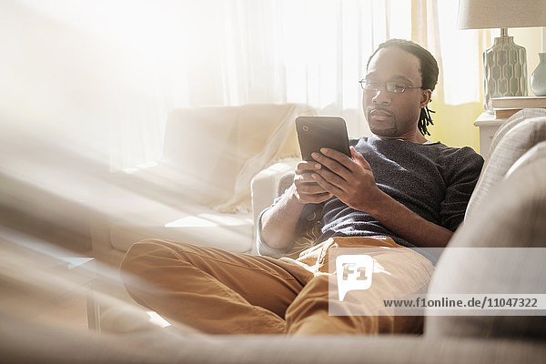 Schwarzer Mann benutzt digitales Tablet auf Sofa