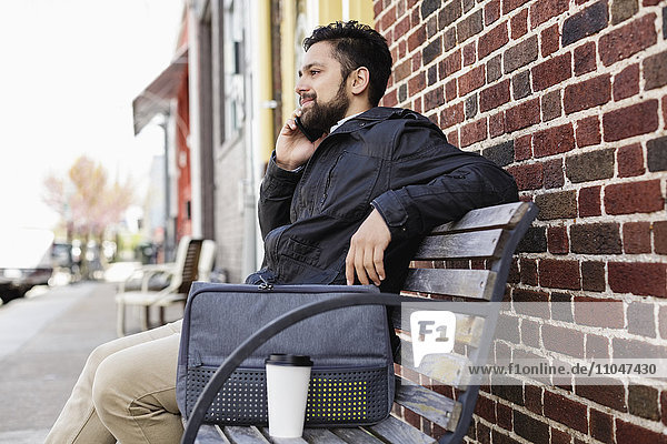 Hispanischer Mann sitzt auf einer Stadtbank und benutzt ein Handy