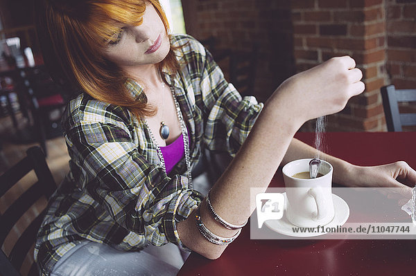 Caucasian woman sprinkling sugar in coffee