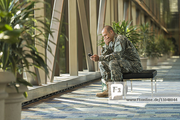 Kaukasischer Soldat benutzt Mobiltelefon im Flughafen