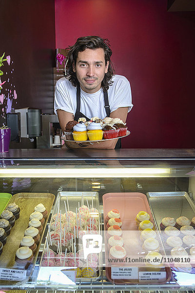 Hispanic business owner showing cupcakes bakery display case