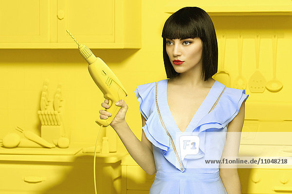 Kaukasische Frau in gelber  altmodischer Küche mit Bohrmaschine