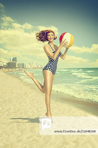 Kaukasische Frau läuft am Strand und trägt einen Strandball