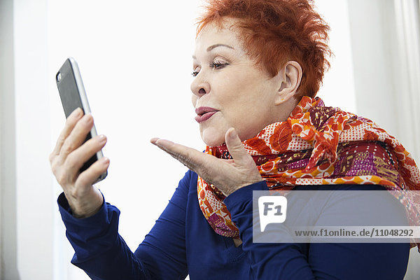 Older Caucasian woman blowing kiss at cell phone