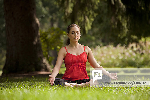 Kaukasische Frau macht Yoga und meditiert auf einem Feld