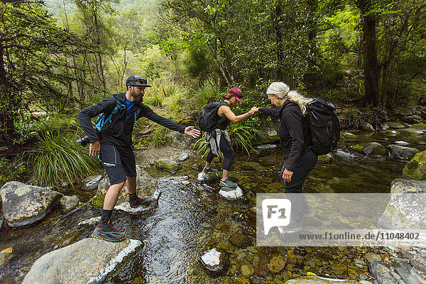 Kaukasische Wanderer überqueren einen Bach auf Felsen im Wald