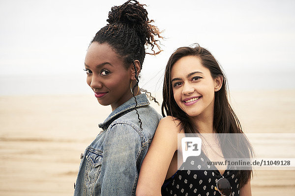 Lächelnde Frauen Rücken an Rücken am Strand