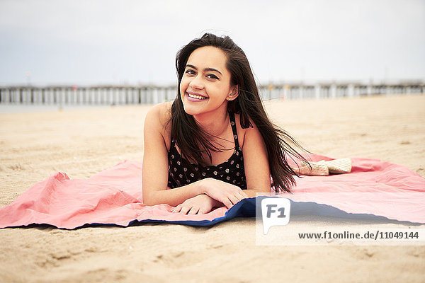 Gemischtrassige Frau liegt auf einer Decke am Strand