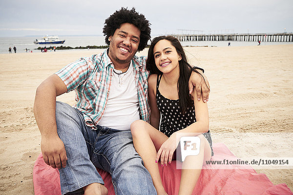 Lächelndes Paar sitzt auf einer Decke am Strand