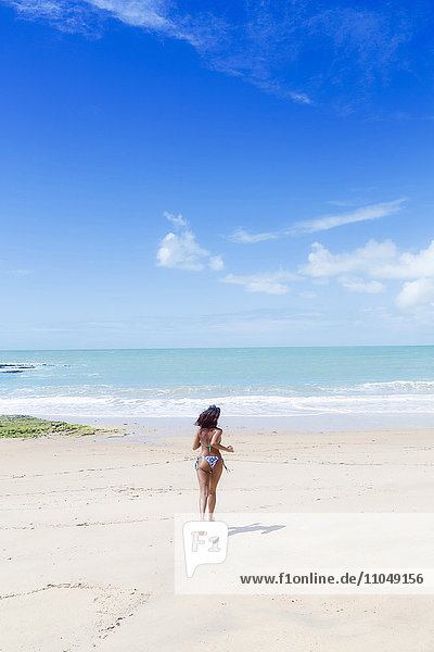 Hispanische Frau läuft am Strand