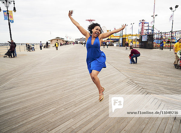 Frau lächelnd und springend auf der Promenade im Vergnügungspark