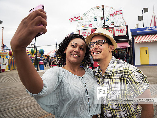 Couple posing for selfie on boardwalk at amusement park