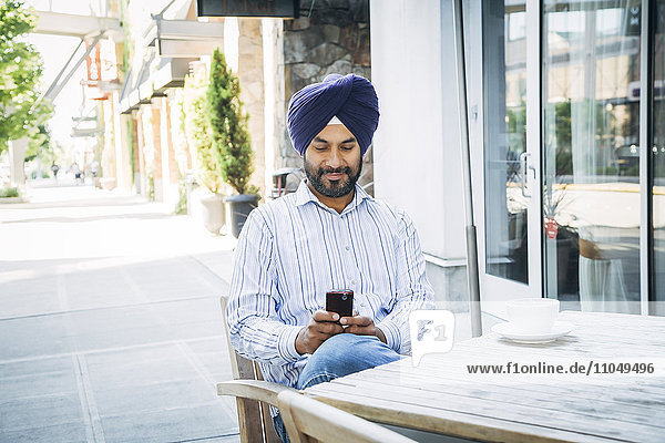 Mann mit Turban  der in einem Café eine SMS auf seinem Handy schreibt