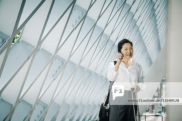 Businesswoman standing in lobby with suitcase talking on cell phone