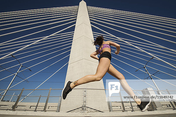 Low angle view of Caucasian woman jogging on urban bridge
