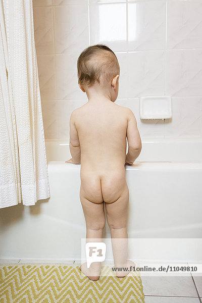 Nacktes kaukasisches Babymädchen in der Badewanne stehend