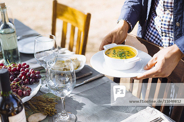 Mann stellt Teller mit Suppe auf einen Tisch im Freien