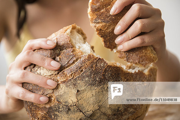 Hispanische Frau reißt runden Laib Brot