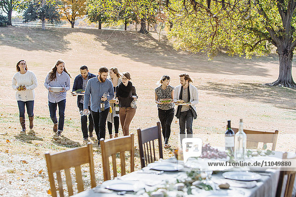 Freunde tragen Essen zu einem Tisch im Freien in einem ländlichen Gebiet