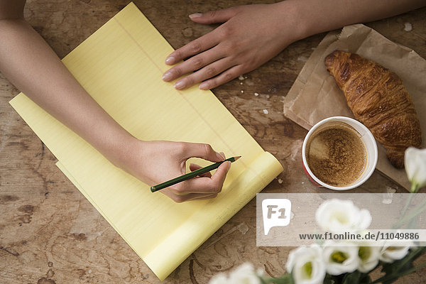 Hispanische Frau schreibt beim Frühstück auf einen gelben Notizblock