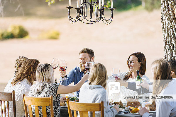 Freunde stoßen am Tisch im Freien mit Wein an