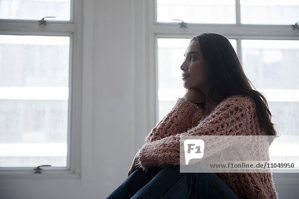 Hispanische Frau in rosa Pullover und Jeans am Fenster