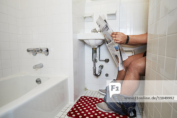 Mixed race man reading newspaper on toilet