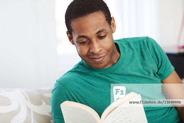 African American man reading book on bed