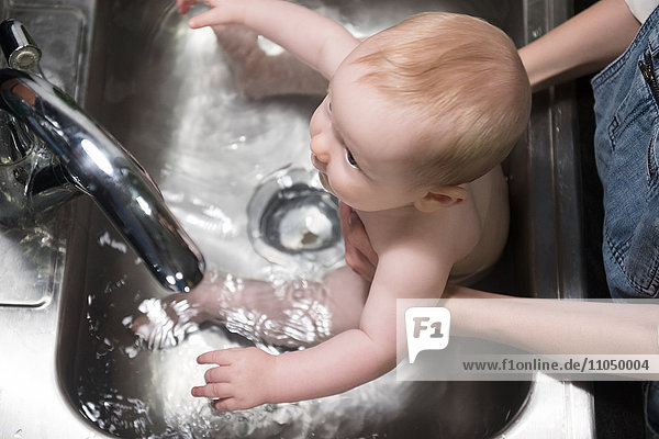 Mutter badet kaukasischen Babysohn im Waschbecken