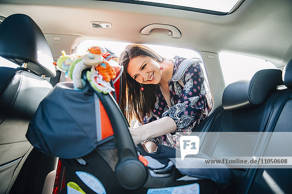 Hispanic mother fastening car seat in car