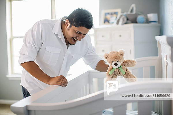 Hispanischer Vater winkt mit Spielzeug für Baby im Kinderzimmer