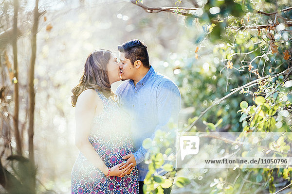 Pregnant Hispanic couple kissing outdoors